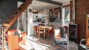 Ein geräumiger Wohnbereich mit einer Holztreppe, einem Esstisch mit Stühlen, einem Kamin und einem großen Fenster mit Aussicht.