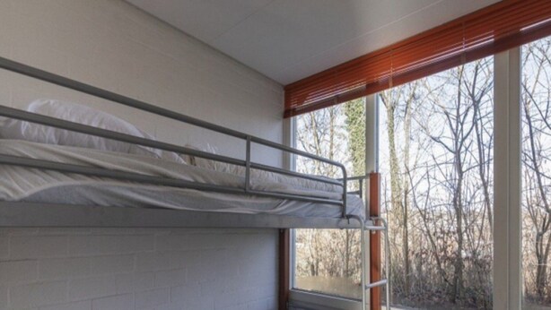 Ein Schlafsaalzimmer mit Etagenbetten, einem Fenster mit Blick auf Bäume und einer Heizung.
