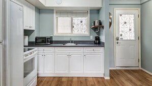 A compact kitchen with white cabinets, a microwave, a coffee maker, and a sink. - Stunning Mountain View Cozy Studio for Small Grp (Canmore)
