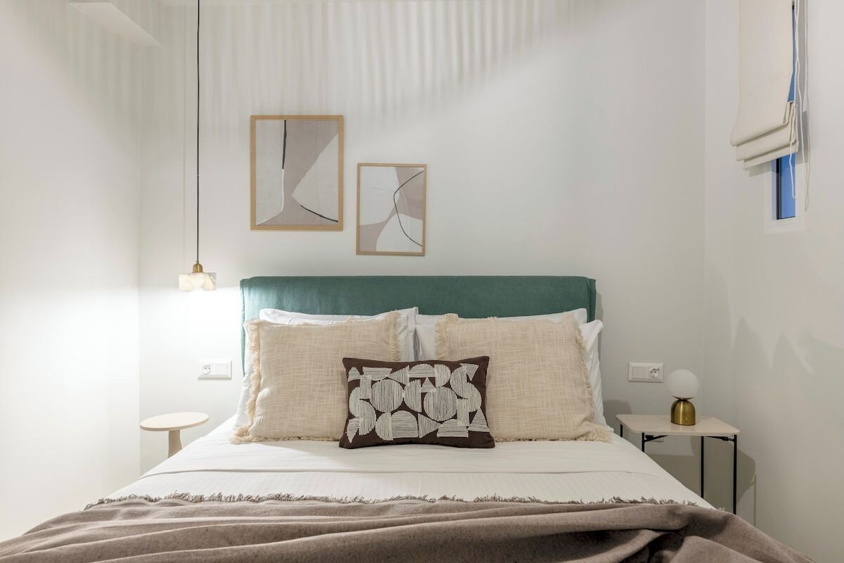 A neatly arranged bedroom with a bed, pillows, a bedside table, and wall art.