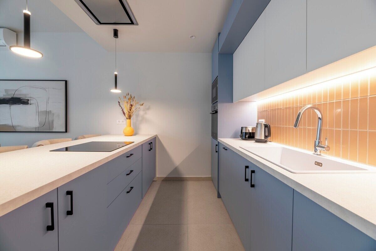 A modern kitchen with a white countertop, grey cabinets, and a tiled backsplash.