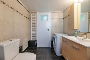 Ein kleines Badezimmer mit Toilette, Waschmaschine, Waschbecken mit Spiegel und Handtuchhalter.