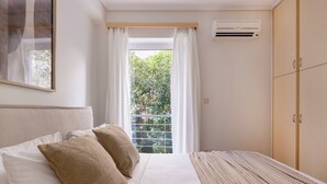A bedroom with a bed, white curtains, a window with a view of greenery, and a wardrobe. - Marousi 2BR Prestige Apartment (Marousi)