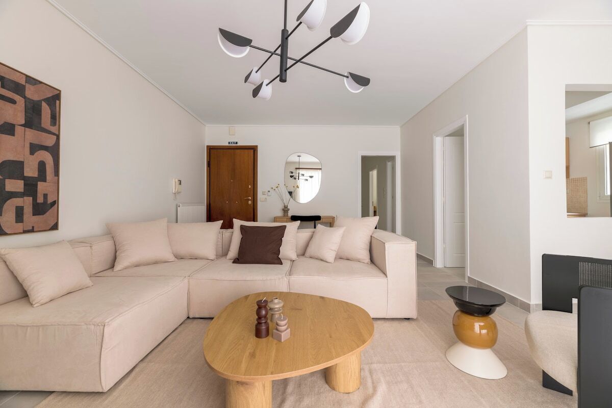 Ein modernes Wohnzimmer mit einem beigefarbenen Ecksofa, einem Holztisch und einer schwarz-weißen Stehlampe.