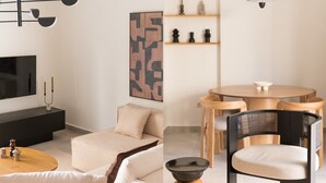 A modern living room with a sofa, a coffee table, a TV, and a dining area with a table and chairs. - Marousi 2BR Prestige Apartment (Marousi)