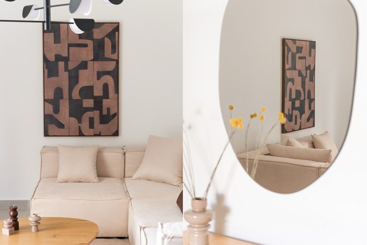 Una sala de estar moderna con un sofá seccional color beige, una mesa de centro redonda de madera y arte abstracto en la pared.