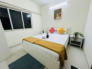Een hotelkamer met een bed, nachtkastje, een kamerplant en een raam.
