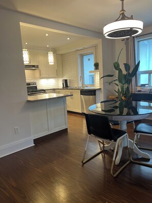 A modern kitchen with white cabinetry, a central island, and a dining area with a glass table and chairs.