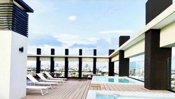 Un área de piscina en la azotea con sillones de descanso y vistas del horizonte de la ciudad.