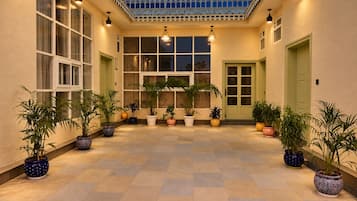 Un espacio al aire libre techado, con plantas en macetas, piso de baldosas y techo decorado.