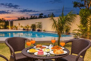 A dining table with plates of food and drinks, a pool in the background, and a sunset sky. - Free Birds Boutique Stay Amer, Jaipur (Amer)