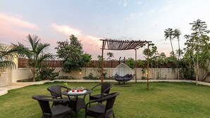 A backyard with a round table, four wicker chairs, a hanging chair, and a pergola. - Free Birds Boutique Stay Amer, Jaipur (Amer)