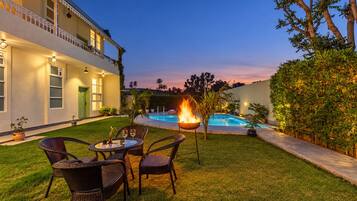 A poolside area with a fire feature, outdoor seating, and a building with a balcony.