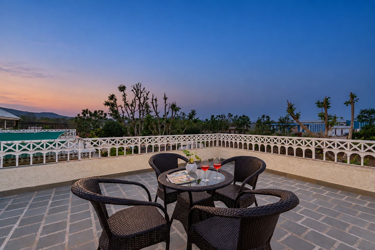 Una terraza con mobiliario de mimbre y una mesa, con vistas a un paisaje con árboles y edificios.