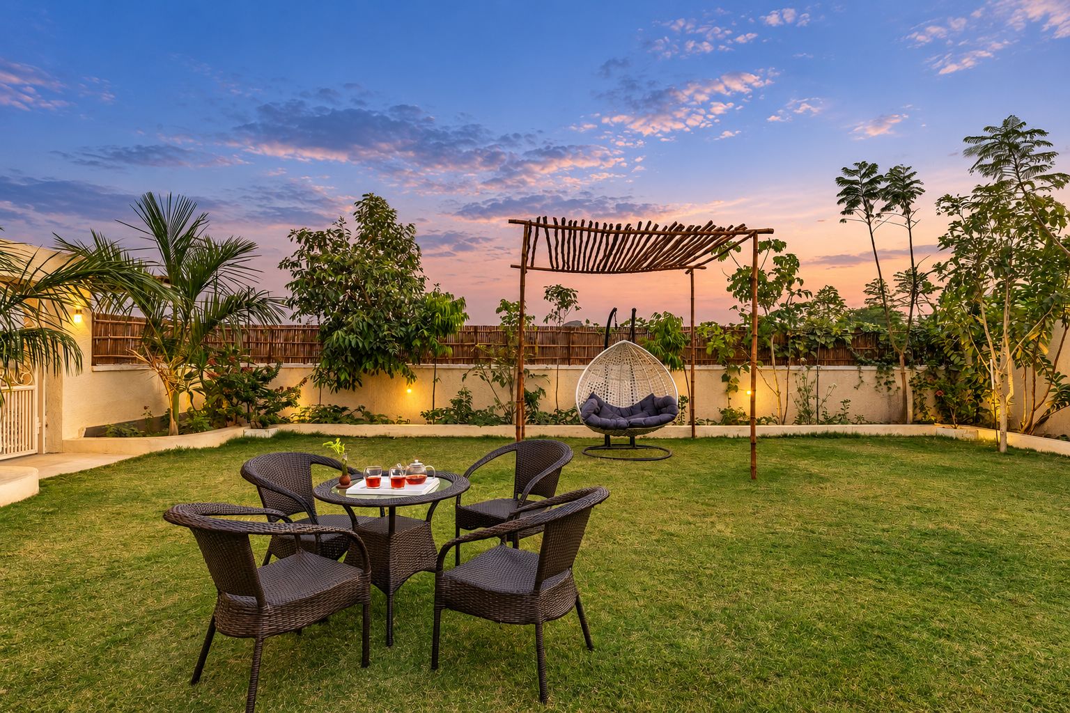 A patio with wicker furniture, a hanging chair, and a table with drinks.