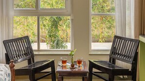 A room with a bed, two wooden chairs, a small table with two glasses of tea, and a window with a view of greenery. - Free Birds Boutique Stay Amer, Jaipur (Amer)