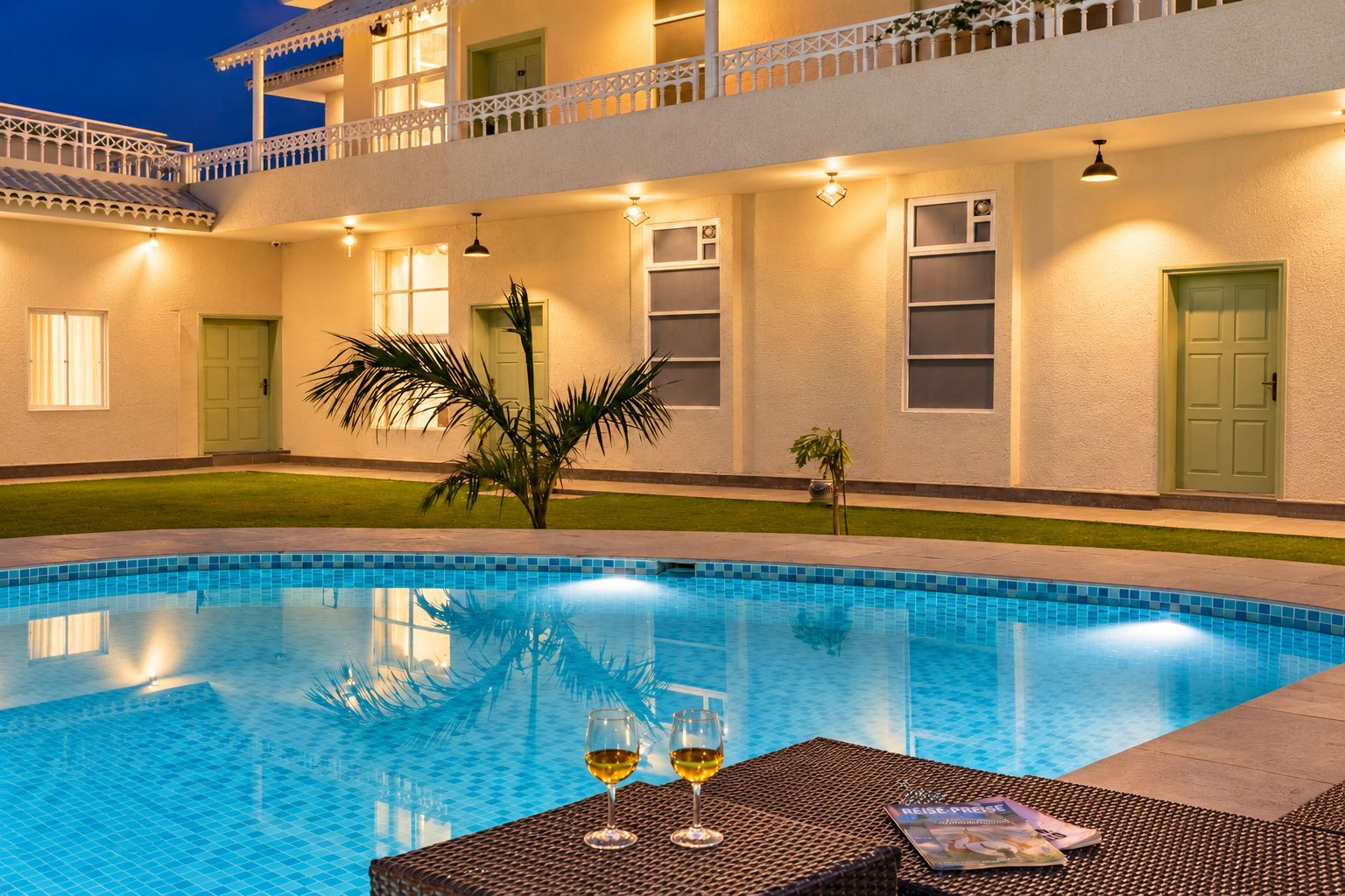Una piscina con mesa y sillas de vidrio, rodeada por un edificio con balcones y ventanas.