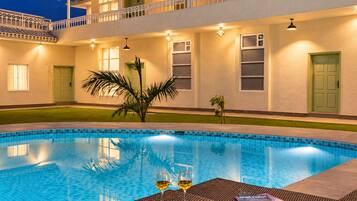 Una piscina con mesa y sillas de vidrio, rodeada por un edificio con balcones y ventanas.