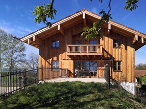 A wooden chalet with a balcony, large windows, and a fenced yard. - Vacation Apartment 1 with a terrace for up to 6 people (Seeon-Seebruck)