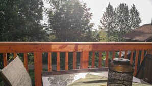 Eine Holzterrasse mit einem für zwei Personen gedecktem Tisch, einer Laterne und einem Stuhl.