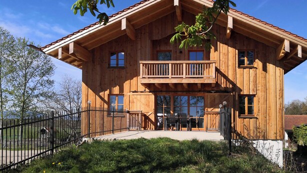 Eine Holzhütte mit Balkon, großen Fenstern und einem eingezäunten Hof.