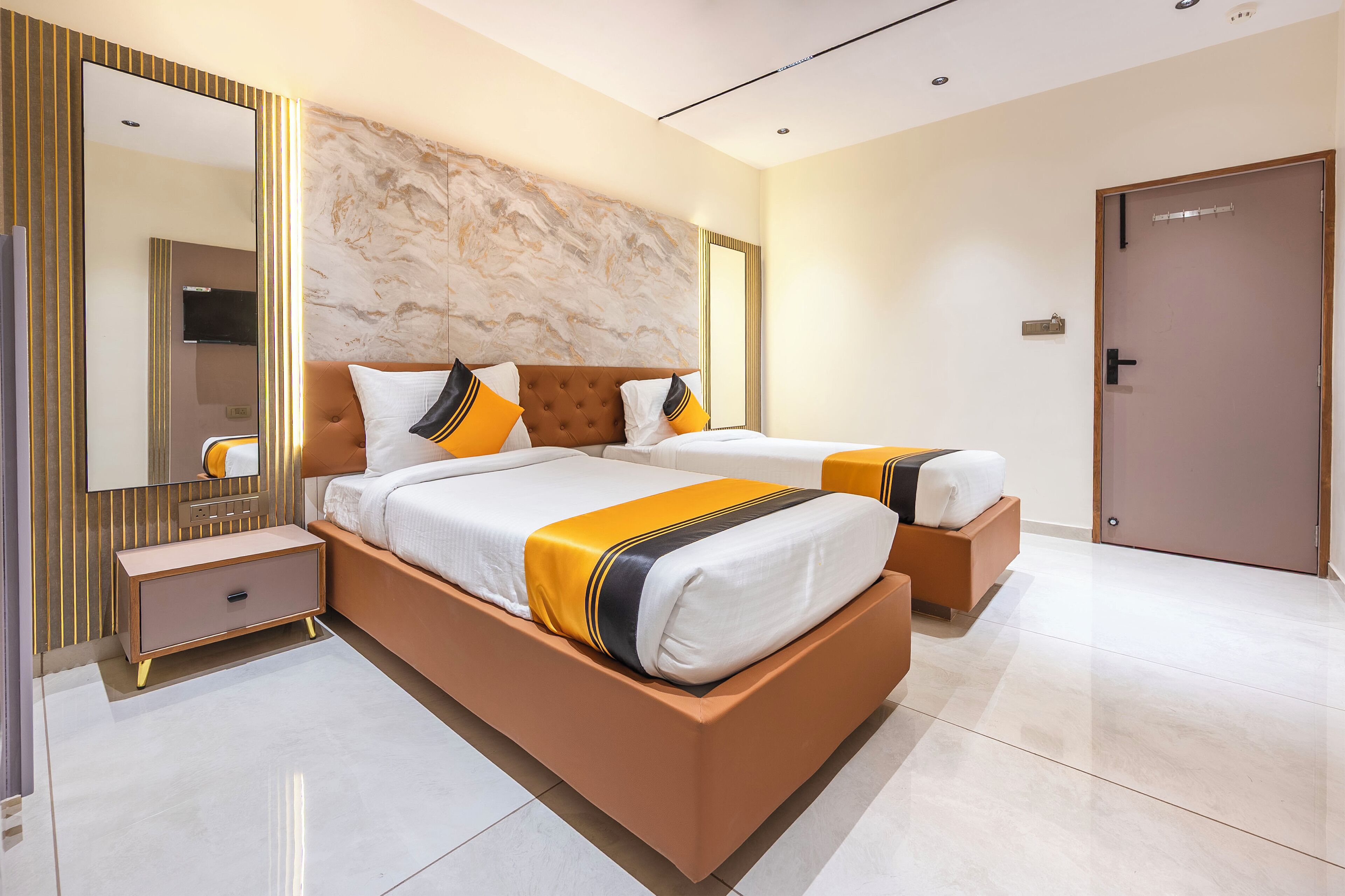 A modern hotel room with a large bed, a bedside table, a mirror, and a door.