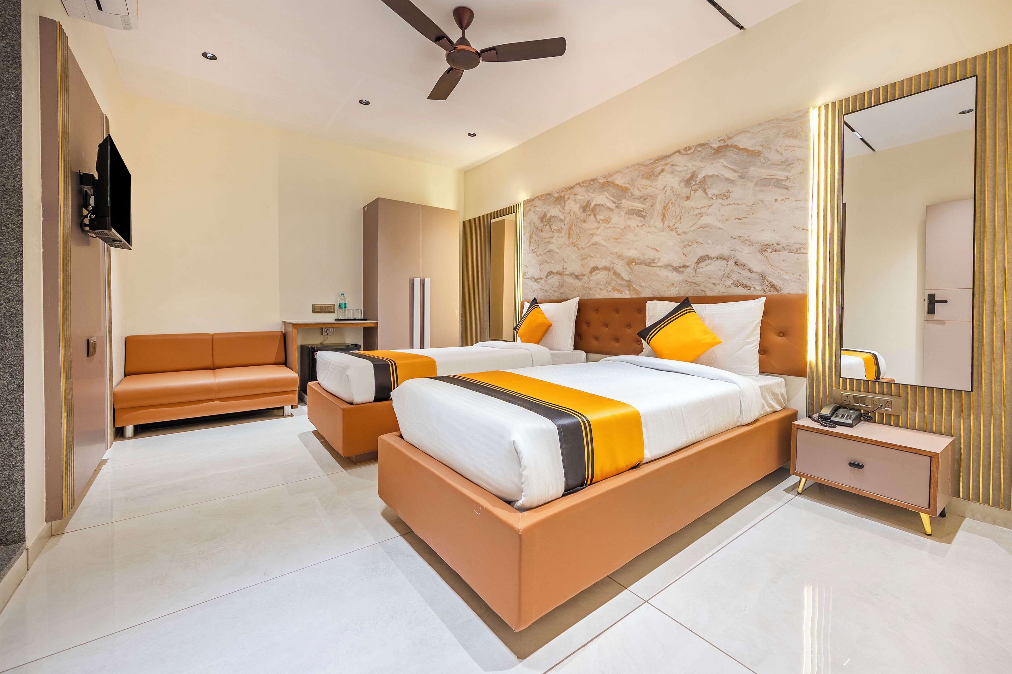 A modern bedroom with a large bed, a sofa, a bedside table, and a ceiling fan.