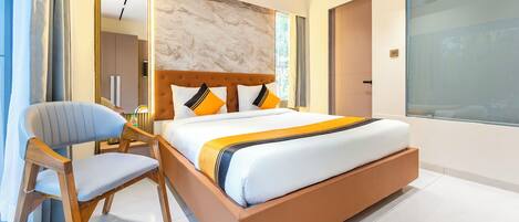 Una habitación de hotel moderna con una cama grande, una silla de madera, un espejo y un ventanal amplio.