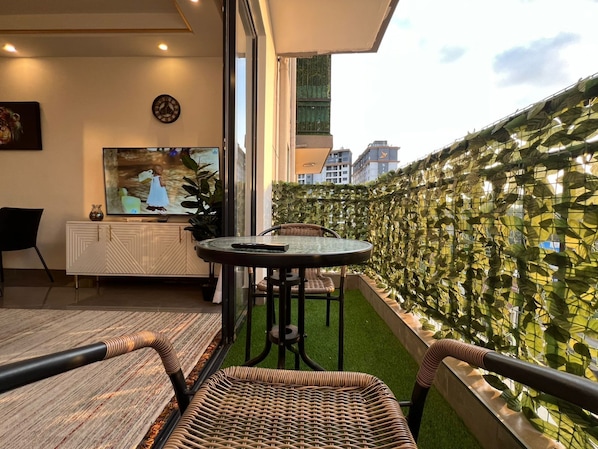 Ein Balkon mit Korbmöbeln, einem Fernseher und Blick auf die Stadt.