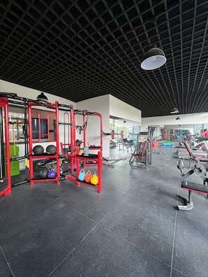 Ein Fitnessraum mit unterschiedlicher Trainingsausstattung, darunter eine rote Hantelbank und Kettlebells.