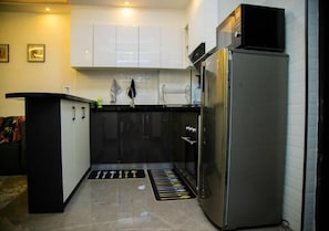 Eine kleine Küche mit weißen Schränken, einer schwarzen Arbeitsplatte und einem Edelstahlkühlschrank.