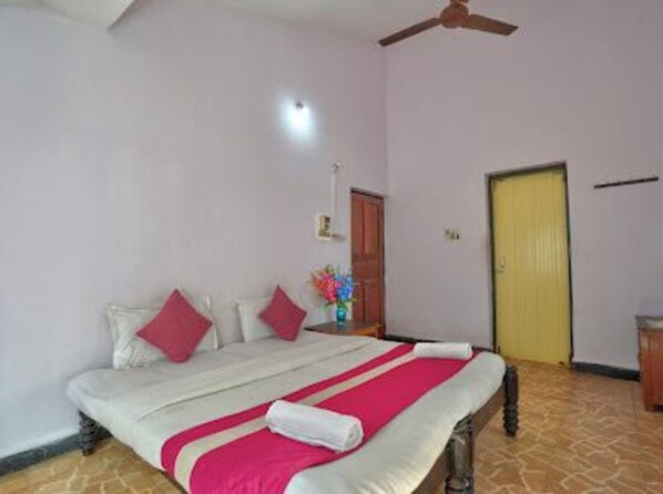 A hotel room with a bed, a ceiling fan, a door, and a small table with a vase of flowers. - Delma's Guest House (Baga)
