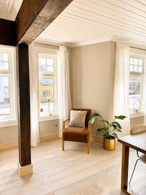 Une pièce avec un plafond orné de poutres en bois, un fauteuil marron avec un coussin, une table et une plante en pot.