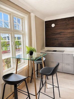 Une cuisine moderne avec une table à manger en verre et deux chaises, une plante en pot et une vue sur l’extérieur.
