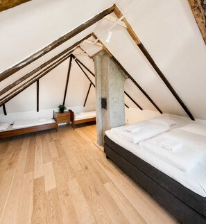 Un dormitorio tipo loft con techo inclinado, vigas de madera, un pilar de hormigón y dos camas.
