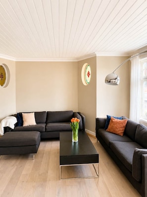 Un salon moderne avec un canapé d’angle, une table basse et des éléments décoratifs, comme une horloge murale et un lampadaire.