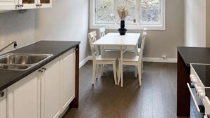 Et køkken med hvide skabe, et spisebord med stole, et vindue med udsigt og en loftlampe.