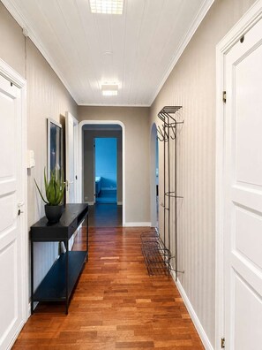 Un pasillo con suelo de madera, paredes blancas y una puerta que da a otra habitación.