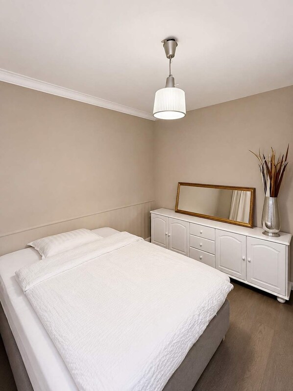 Un dormitorio con cama, cómoda, espejo y lámpara colgante.