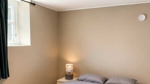 A bedroom with a bed, a bedside table with a lamp, a window with curtains, and a ceiling light.