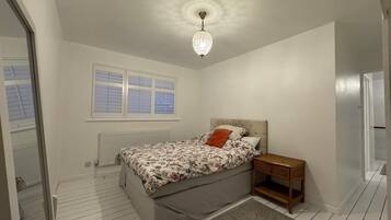 A bedroom with a bed, a nightstand, a window with blinds, a radiator, and a chandelier.