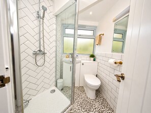 Une salle de bain moderne équipée d’une douche, de toilettes et d’un lavabo, avec un carrelage disposé en motif chevrons et une cabine de douche en verre.
