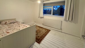 Een slaapkamer met een bed, een radiator, een raam met gordijnen en een hanglamp.