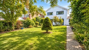 Une pelouse bien entretenue, avec un petit arbre et un chemin menant à un bâtiment blanc doté de nombreuses fenêtres.