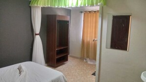 A bedroom with a bed, a wardrobe, a curtain, and a door. - Aldi Jambo Hotel (Homa Bay)