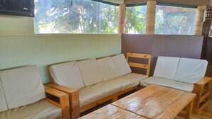 A wooden bench and sofa set in a room with a window overlooking greenery. - Aldi Jambo Hotel (Homa Bay)