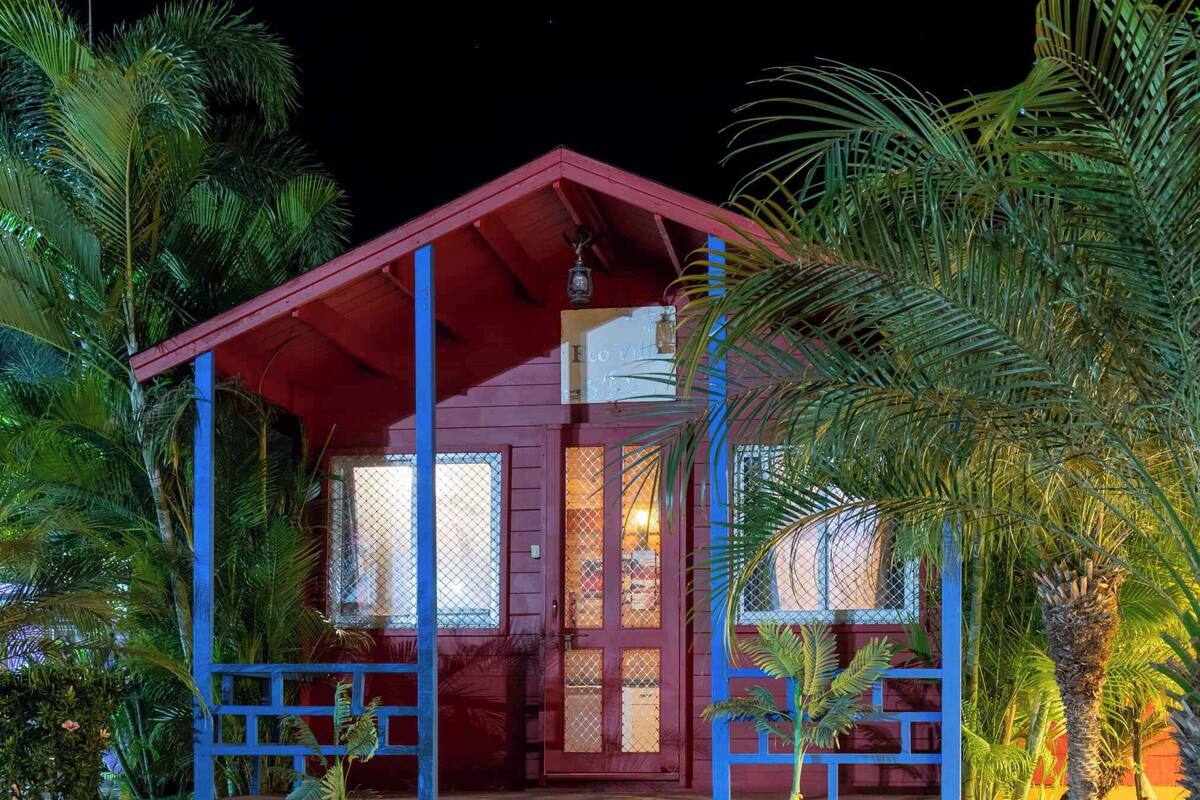 A two-story building with a red roof and blue accents, surrounded by lush greenery.