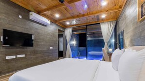 A bedroom with a large bed, wooden ceiling, built-in TV, and a glass door leading to a pool area. - Eco Holiday Resorts (Indore)