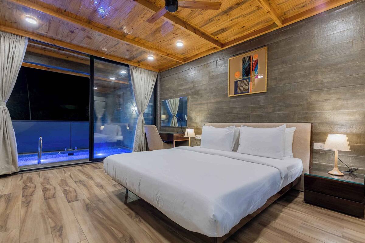 A modern bedroom with a large bed, wooden ceiling, and a glass door leading to a balcony.