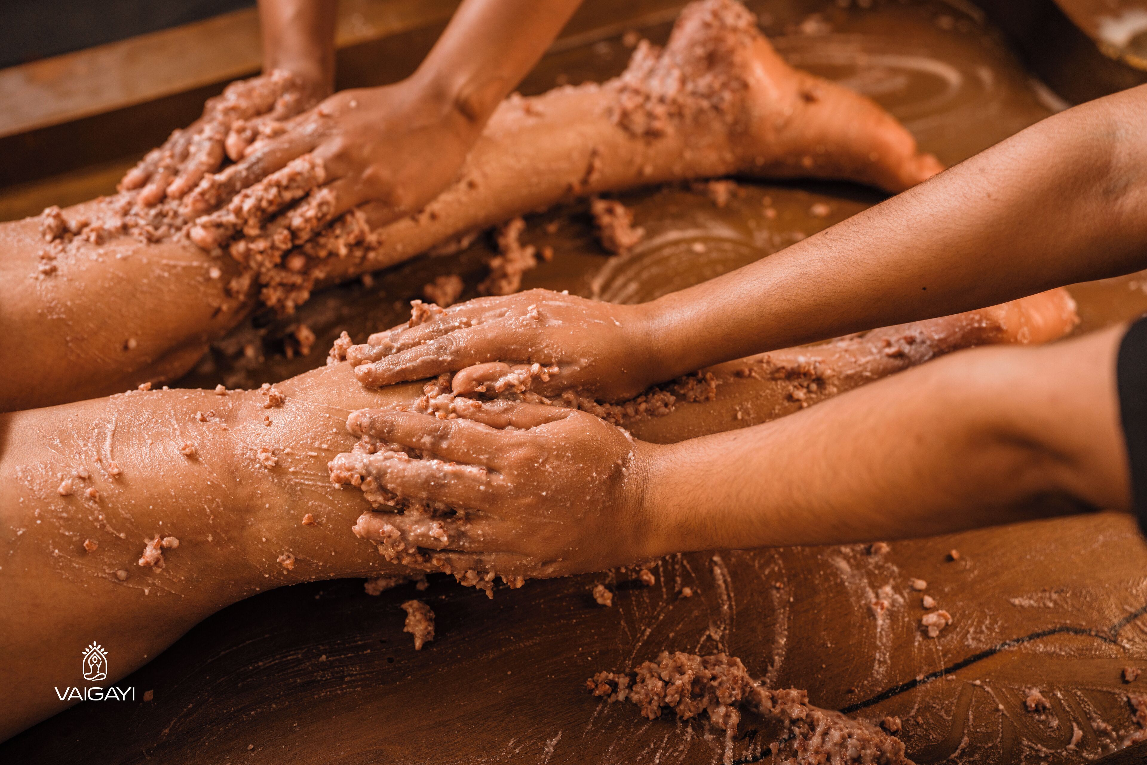 A group of hands covered in a brown substance, possibly a massage or treatment, on a wooden surface.